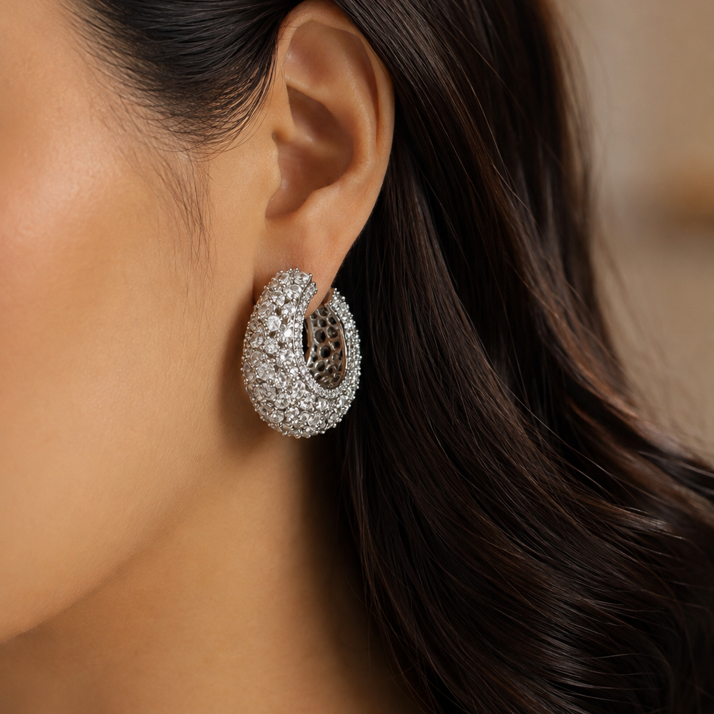 A close-up of a model's ear wearing a silver-toned, diamond-encrusted crescent-shaped hoop earring.