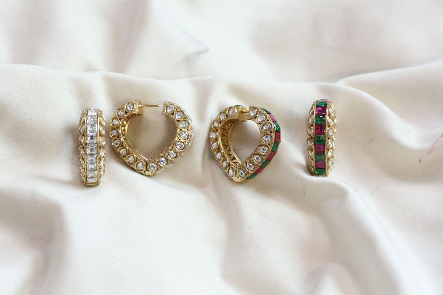 Four gold hoop earrings with different stone and gem embellishments, displayed on a draped white satin fabric background.